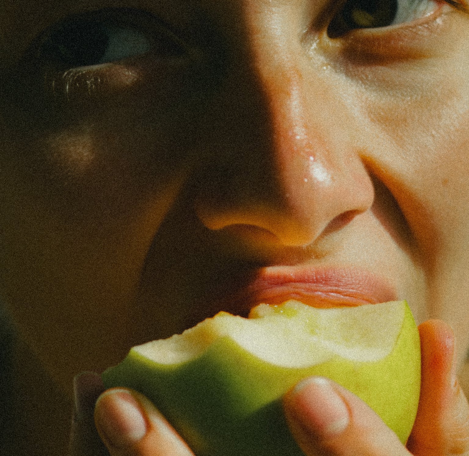 Close-up of a person holding a green apple near their face.